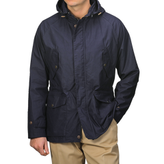 A person wearing L'Impermeabile's Navy Blue Waxed Cotton Bob Short Parka and beige pants keeps their face hidden with a water-repellant jacket featuring buttoned pockets and a front closure.