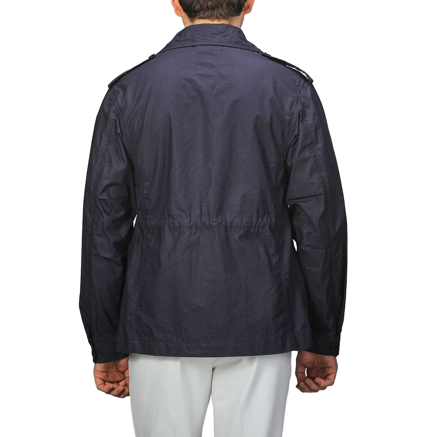 A person wearing a L'Impermeabile Navy Blue Waxed Cotton Smith SFO Jacket with shoulder epaulets, viewed from the back, paired with white pants.