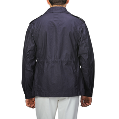 A person wearing a L'Impermeabile Navy Blue Waxed Cotton Smith SFO Jacket with shoulder epaulets, viewed from the back, paired with white pants.