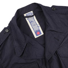 The Navy Blue Waxed Cotton Smith SFO Jacket by L'Impermeabile boasts a button-detailed collar and water-repellent finish. Inside, the label's stylized font and small red emblem enhance its unique appeal.