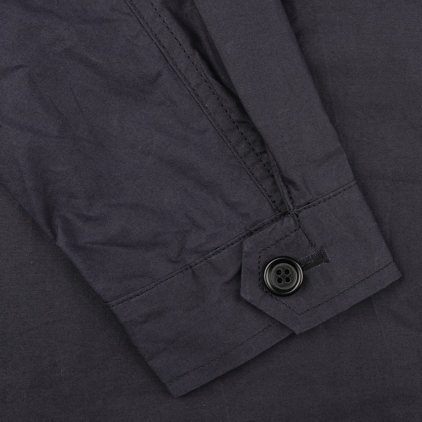 Close-up of a dark fabric sleeve with a black buttoned cuff, highlighting the refined style of L'Impermeabile's Navy Blue Waxed Cotton Smith SFO Jacket with its water-repellant finish.