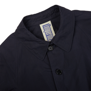 A close up of a L'Impermeabile navy blue waxed cotton Kamikaze trenchcoat on a white background.