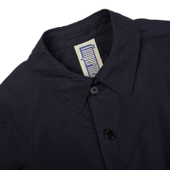 A close up of a L'Impermeabile navy blue waxed cotton Kamikaze trenchcoat on a white background.