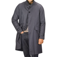 A person wearing a washed blue waxed cotton Kamikaze Coat by L'Impermeabile, one hand in their pants pocket. Their face is not visible.