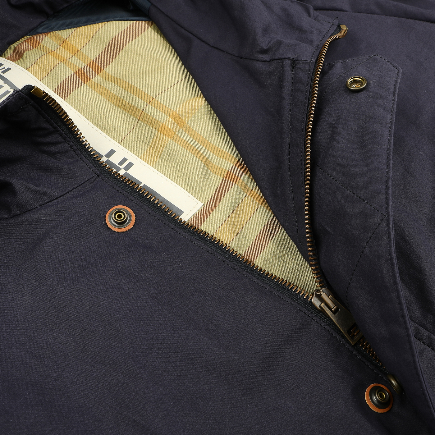 A close-up of the L'Impermeabile Navy Blue Waxed Cotton Bob Short Parka with zipper and button detail reveals a beige plaid lining inside.