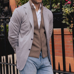 A man standing by a fence, wearing a Light Grey Houndstooth Cotton Jersey Canali blazer, white shirt, and blue jeans.