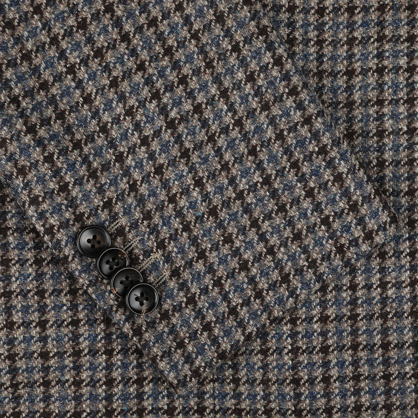 Close-up of a houndstooth patterned fabric, showcasing a sleeve featuring four black buttons on the Brown Houndstooth Wool Cashmere Hybrid Blazer by Luigi Bianchi, crafted with luxurious tailoring in pure virgin wool.