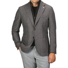 A person wearing a Luigi Bianchi brown houndstooth wool cashmere hybrid blazer over a black top, with grey pants. Their right hand is in their pocket. The person's head is not visible in the image.