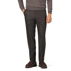 A person is wearing a long-sleeved grey sweater, dark brown wool flannel flat front trousers from Luigi Bianchi, and brown dress shoes. Hands are in the pockets of the trousers; the head is not visible in the image.