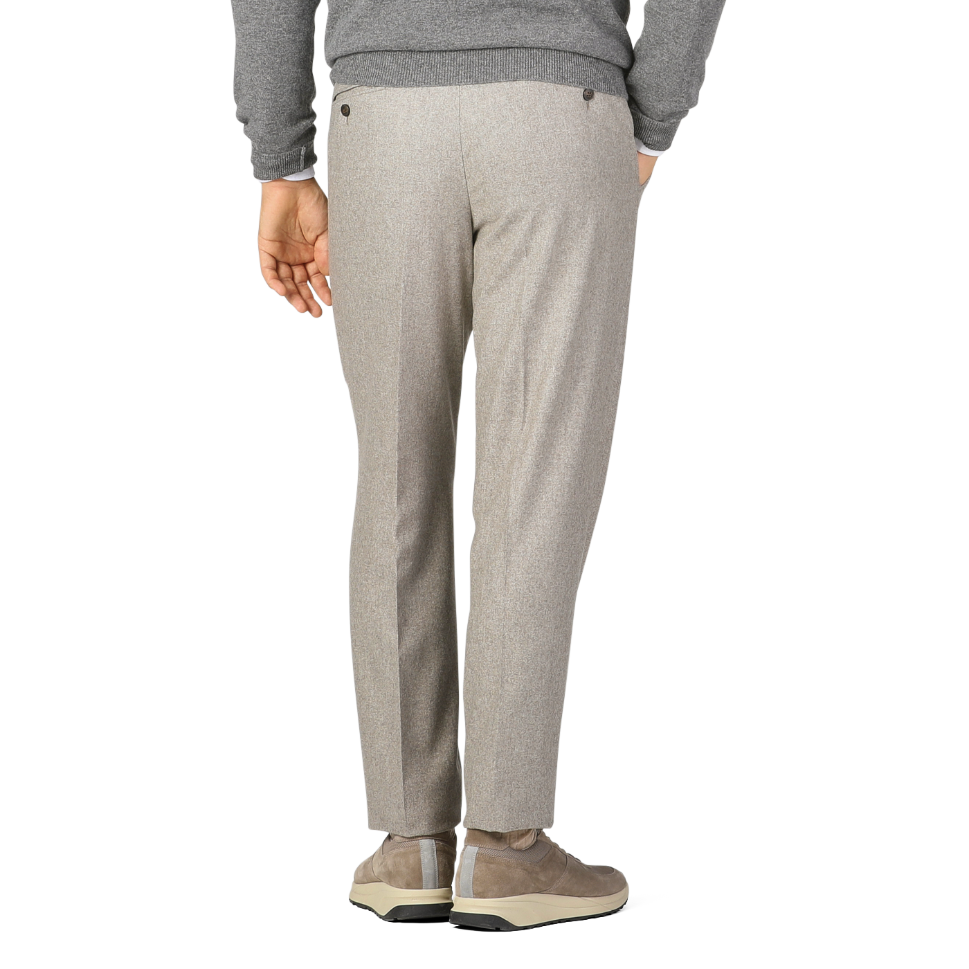 Person wearing oatmeal beige Luigi Bianchi wool flannel flat front trousers, a gray sweater, and beige sneakers stands with one hand in their pocket, facing away from the camera.