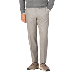 A person dressed in a grey sweater and Luigi Bianchi Oatmeal Beige Wool Flannel Flat Front Trousers is standing with one hand in their pocket. The person is also wearing beige sneakers. Only the lower half of the body is visible.