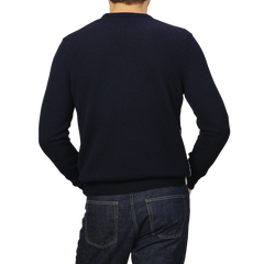 A person is wearing a Navy Blue Wool Cashmere Cortina Sweater from MC2 Saint Barth paired with jeans, capturing the cozy elegance of an Apres Ski Collection, seen from behind against a plain background.