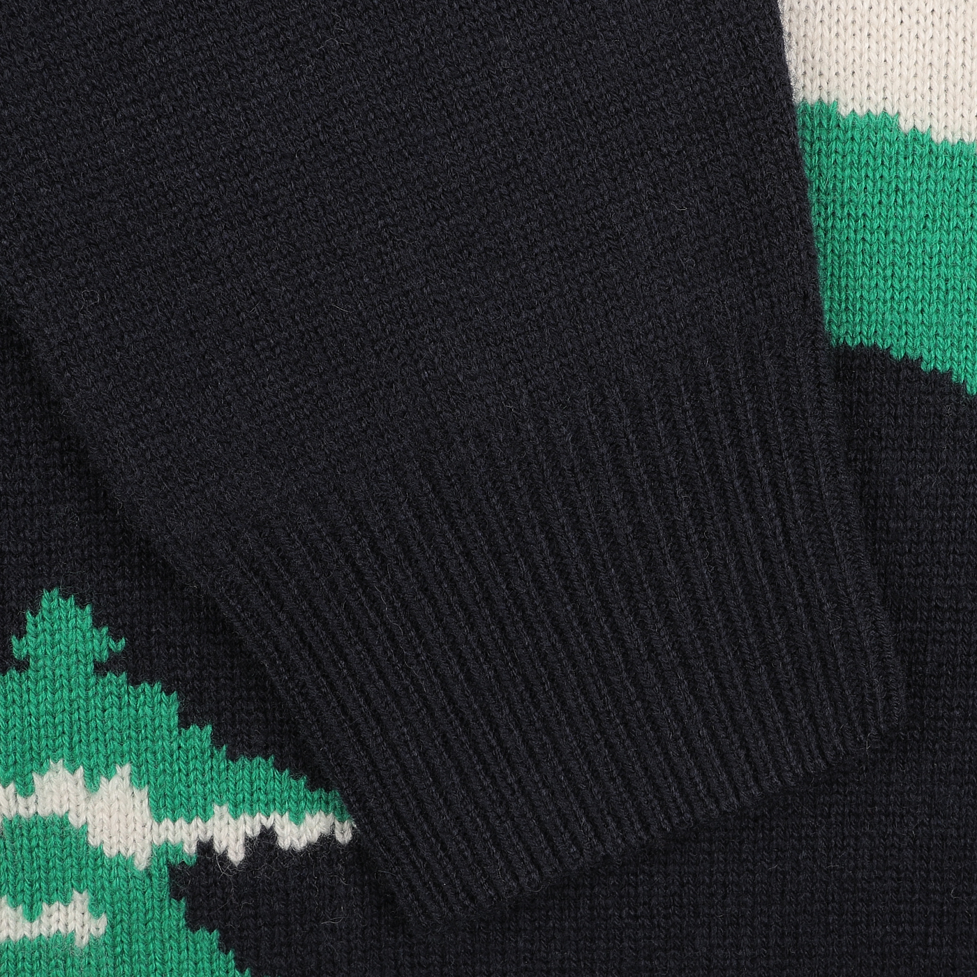 Close-up of a knitted navy blue sweater with a ribbed cuff, showcasing green and white patterns inspired by the Cortina ski resorts in Italy. Ideal for the Après Ski Collection from MC2 Saint Barth.