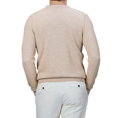 A person wearing the Beige Wool Cashmere Courchevel Sweater by MC2 Saint Barth combined with white pants is shown from the back against a plain background, capturing the cozy elegance of the Après Ski Collection—ideal for winter afternoons at ski resorts.