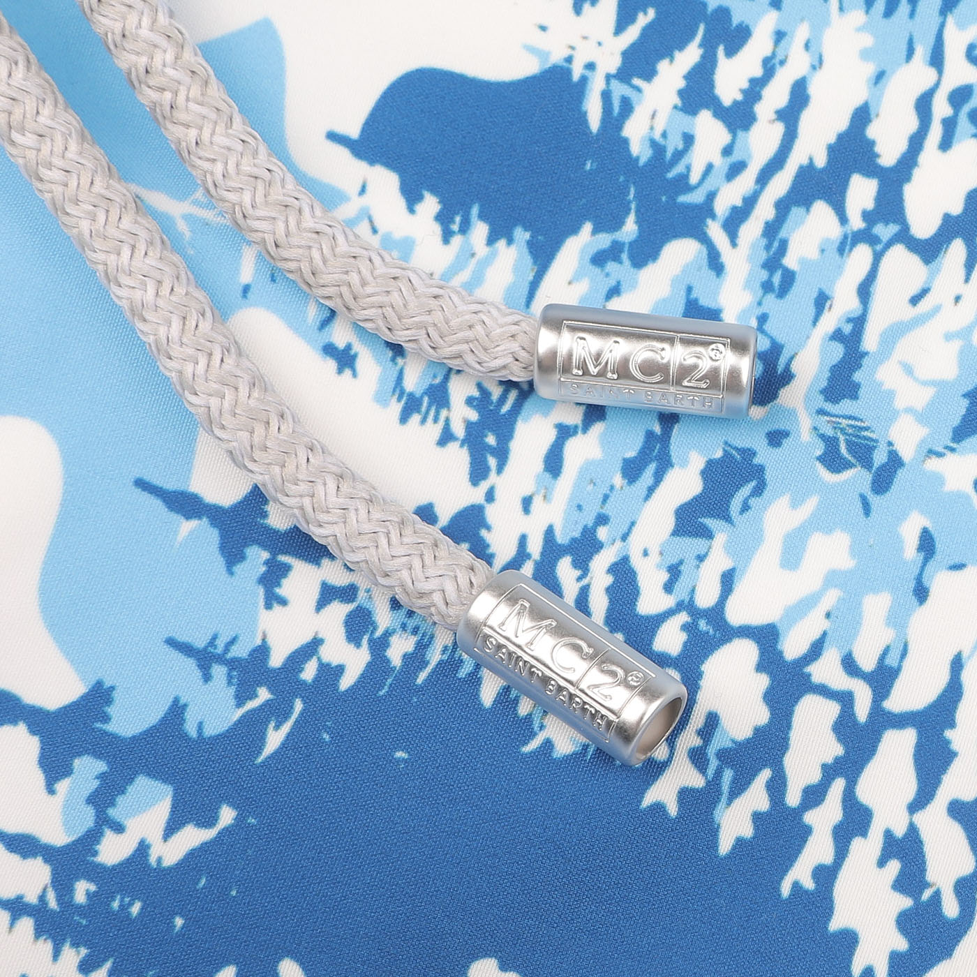 Close-up of two gray braided drawstrings with metallic tips labeled "MC2 Saint Barth" on the Blue St. Moritz Printed Swim Shorts, crafted from quick-drying fabric.