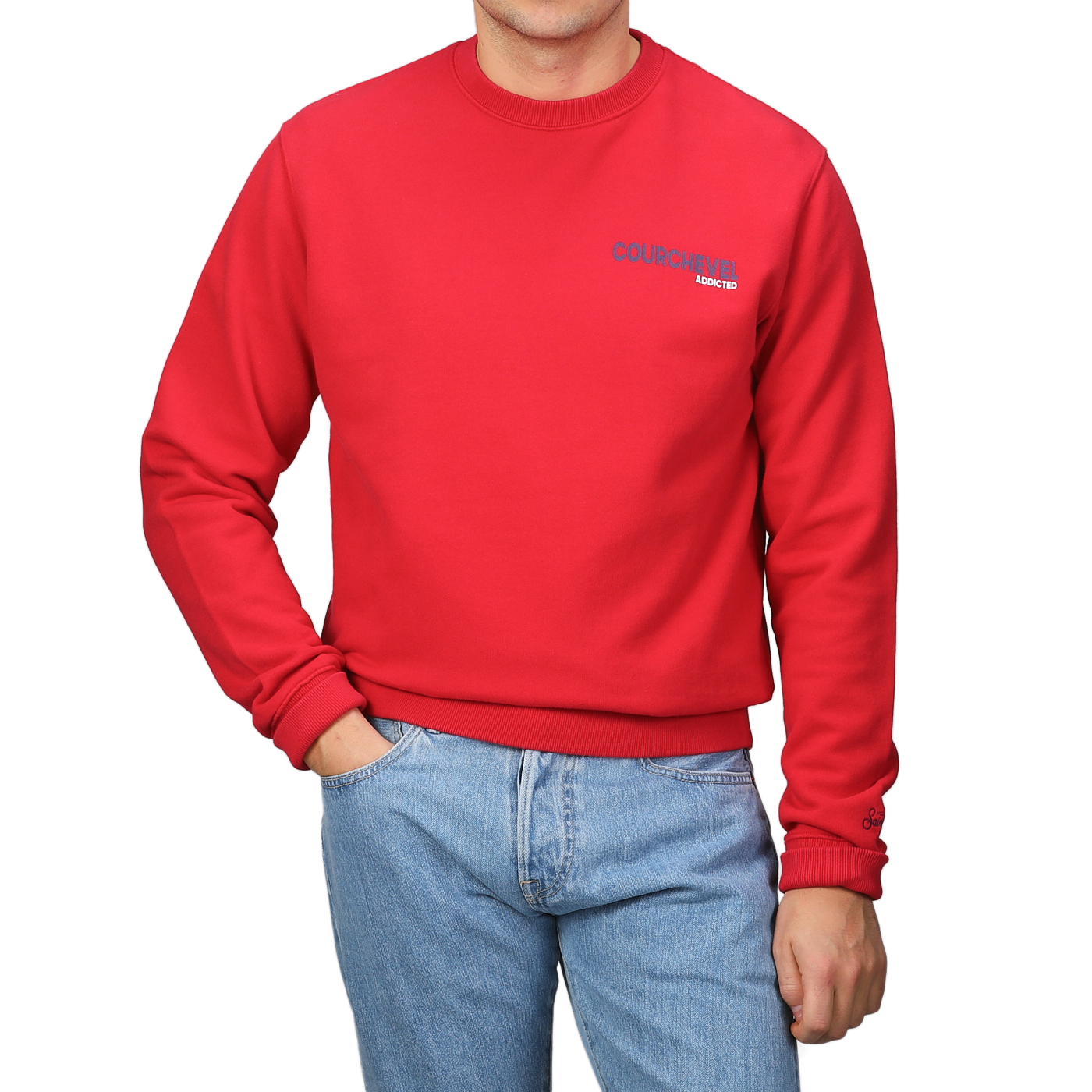 Wearing an MC2 Saint Barth Bright Red Cotton Courchevel Sweater adorned with text and blue jeans, a person stands against a gray background, perfectly capturing the relaxed spirit of Courchevel's après-ski scene.