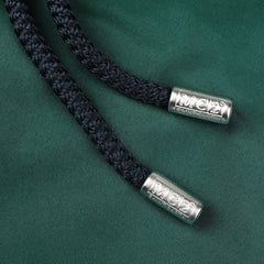 Close-up of two black drawstrings with metallic tips labeled "MC2 Saint Barth" on a British Green Pantone 18-5315 Swim Shorts fabric background.