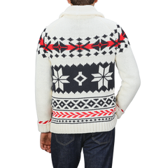 A person is seen from the back, wearing a Cream White Wool Nordic Aztec Cardigan by MC2 Saint Barth. The sweater features a white and black patterned design with red accents, paired with a shawl collar, all crafted from a cozy wool-blend. This stylish piece embodies the aesthetic of an Archer Nordic Aztec cardigan.