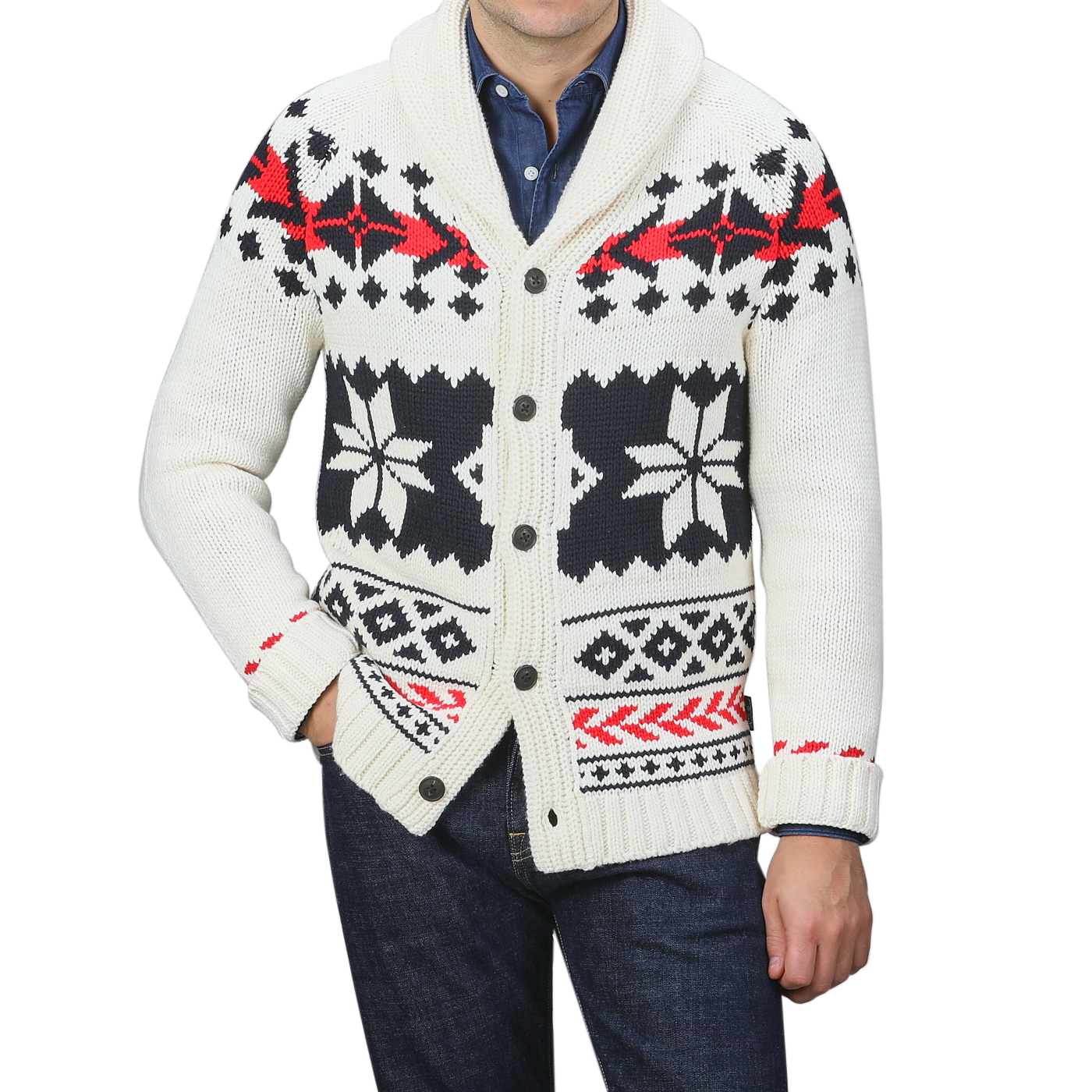 A person is wearing an MC2 Saint Barth Cream White Wool Nordic Aztec Cardigan with a shawl collar, showcasing a black and red geometric pattern against a cream base, elegantly layered over a blue shirt and dark jeans.