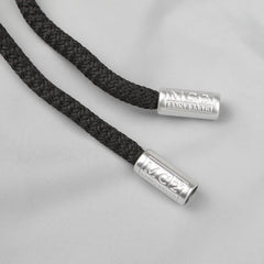 The image shows a close-up of two black braided cords with silver metallic ends engraved with "MC2 SAINT BARTH" against a light gray background, reminiscent of the sleek design featured in their Light Grey Pantone 15-4307 Swim Shorts, renowned for their quick-drying fabric.