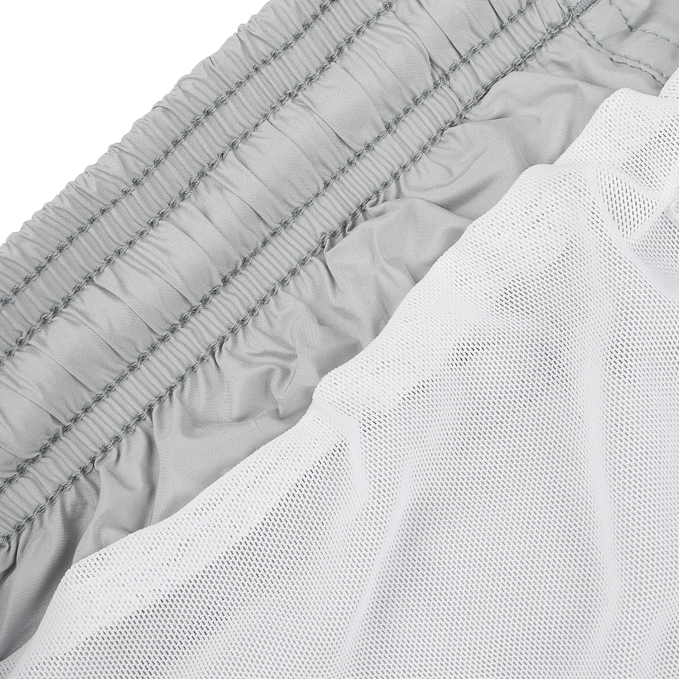 A close-up displays a neatly stacked pile of folded Light Grey Pantone 15-4307 Swim Shorts from MC2 Saint Barth, highlighting their elastic waistbands, positioned beside a folded white mesh fabric. This collection boasts quick-drying material, making it ideal for efficiency and convenience.