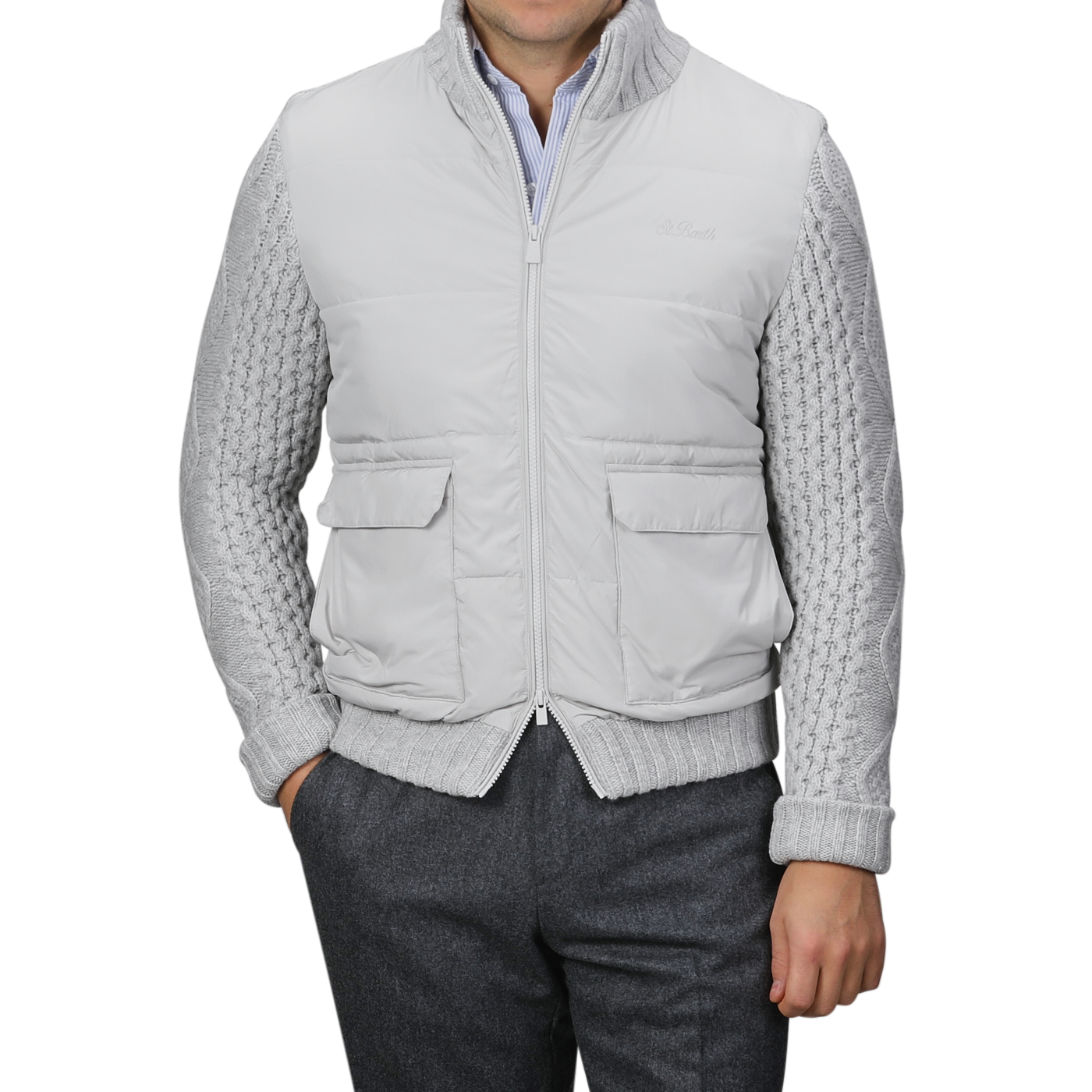 A person wearing an MC2 Saint Barth Light Grey Wool Whistler Padded Jacket over a gray cable-knit sweater and dark gray pants stands against a plain background. The jacket features two front pockets and a zip closure, combining practicality with style.