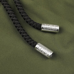 Close-up of two black braided drawstrings with silver metal tips set against the fabric background of the Military Green Pantone 18-0316 Swim Shorts by MC2 Saint Barth, highlighting a contrasting drawstring waist.