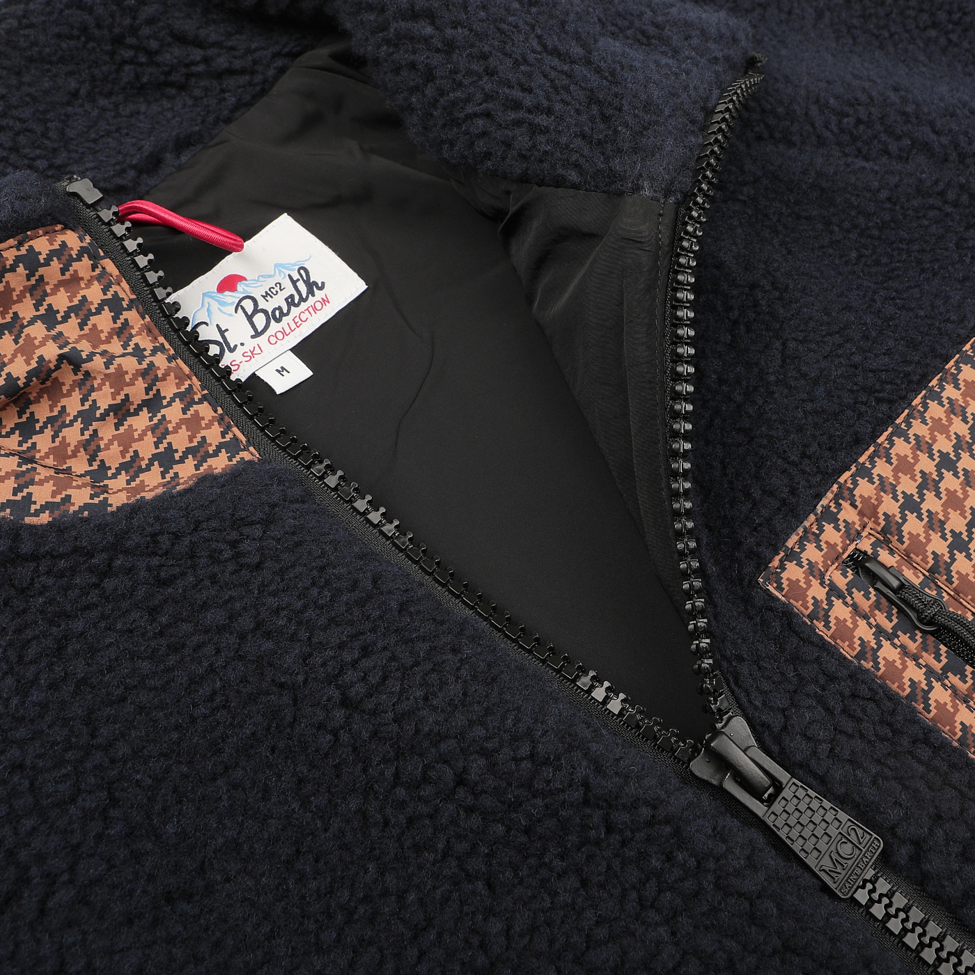 Close-up of the MC2 Saint Barth Navy Blue Sherpa Fleece Jacket featuring camel beige houndstooth pockets, zipped halfway open to show the interior tag labeled "It's a Beach Ski Collection M." The regular fit design offers both comfort and style for any occasion.