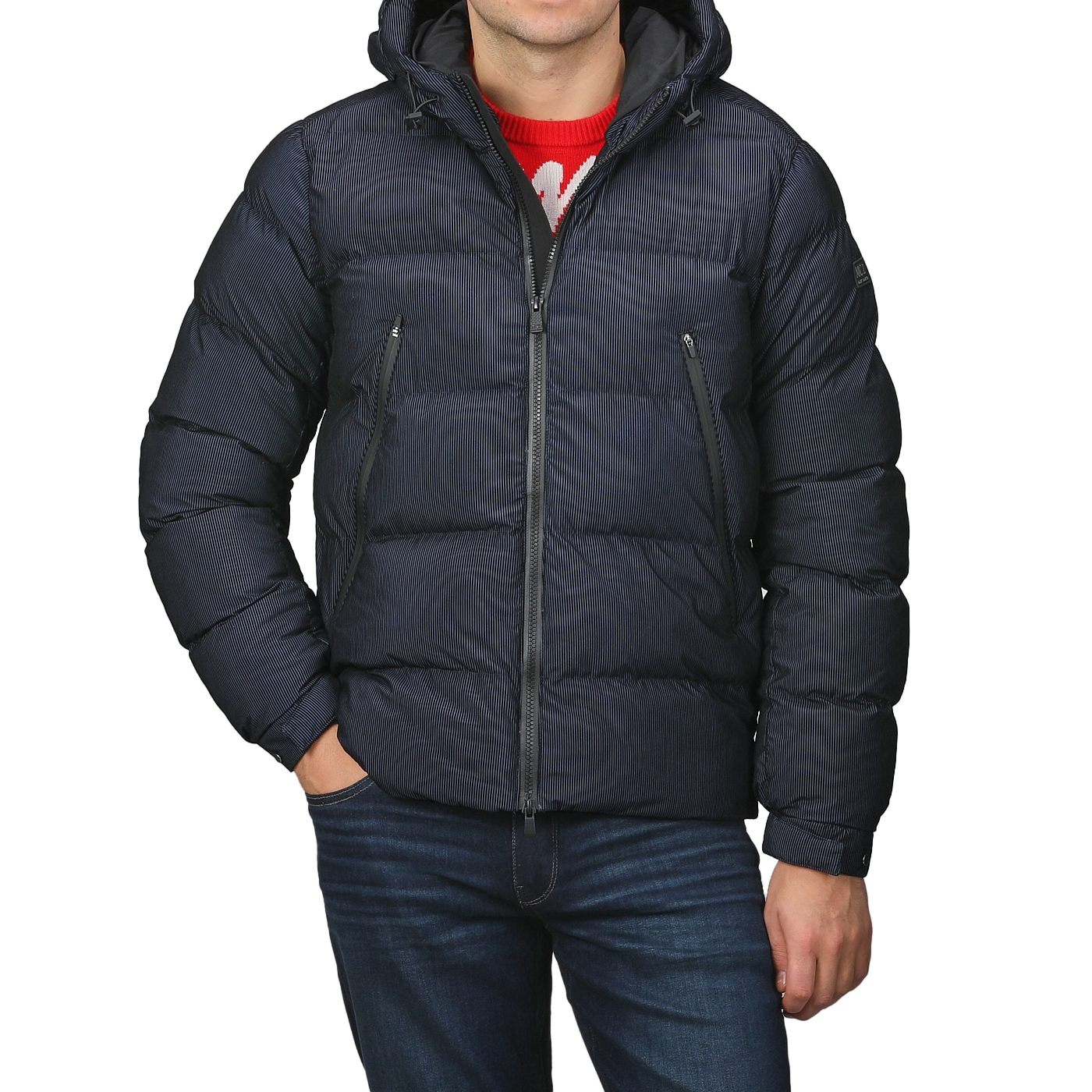 A person stands against a plain background, clad in a Navy Blue Technical Padded Maier Jacket by MC2 Saint Barth with recycled filling, a red sweater, and blue jeans. With hands tucked in pockets, they exude effortless style reminiscent of Saint Barth's casual elegance.