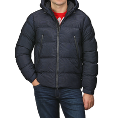 A person stands against a plain background, clad in a Navy Blue Technical Padded Maier Jacket by MC2 Saint Barth with recycled filling, a red sweater, and blue jeans. With hands tucked in pockets, they exude effortless style reminiscent of Saint Barth's casual elegance.