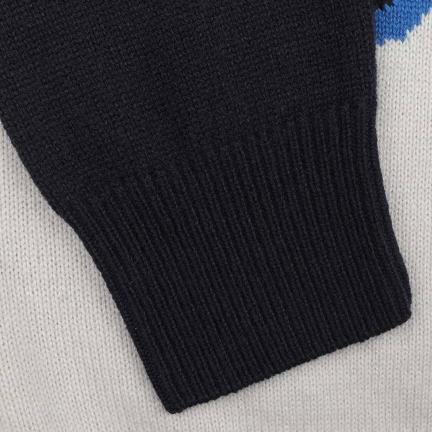 Close-up of a black knit sleeve on the MC2 Saint Barth Navy Blue Wool Cashmere Aprés Ski Sweater, with hints of white and blue fabric, evoking the essence of our Après Ski Collection.