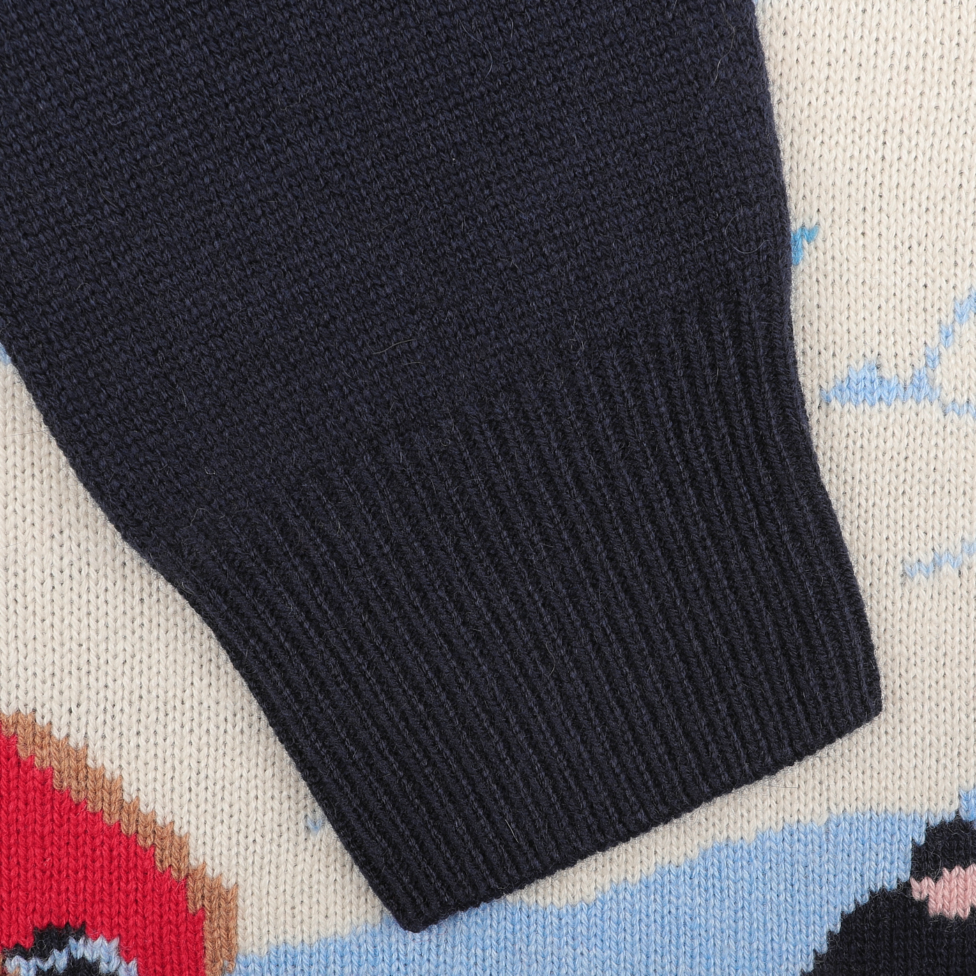 Close-up of the sleeve from the Navy Blue Wool Cashmere Courchevel Sweater by MC2 Saint Barth, set against a colorful knitted background with patterns reminiscent of Courchevel's vibrant ski resorts.