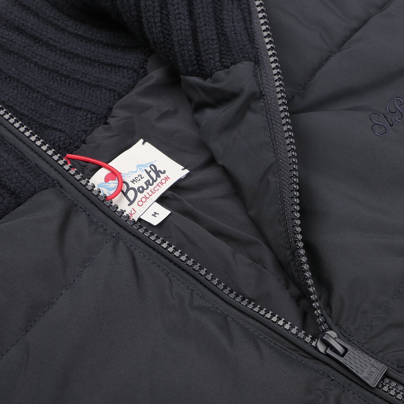 Close-up of a navy blue padded jacket with a visible zipper and a label showing the size "M" from the MC2 Saint Barth collection, offering refined warmth.