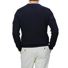 A person wearing the Navy Wool Cashmere Cortina Sweater from MC2 Saint Barth and light-colored pants stands with their back to the camera, channeling the sleek elegance of the Aprés Ski Collection, as if ready to step onto the snowy trails of Cortina, Italy.