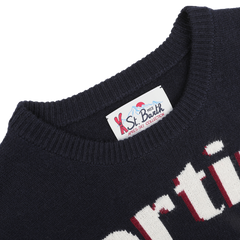 An image highlighting a navy blue sweater with an embroidered design and a label from the "MC2 Saint Barth" brand, part of their "Navy Wool Cashmere Cortina Sweater," ideal for relaxing evenings after skiing at resorts such as Cortina in Italy.