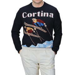 A person stands against a plain background, wearing white pants and the MC2 Saint Barth Navy Wool Cashmere Cortina Sweater, highlighting the spirit of Cortina Italy's ski resorts from the Après Ski Collection.