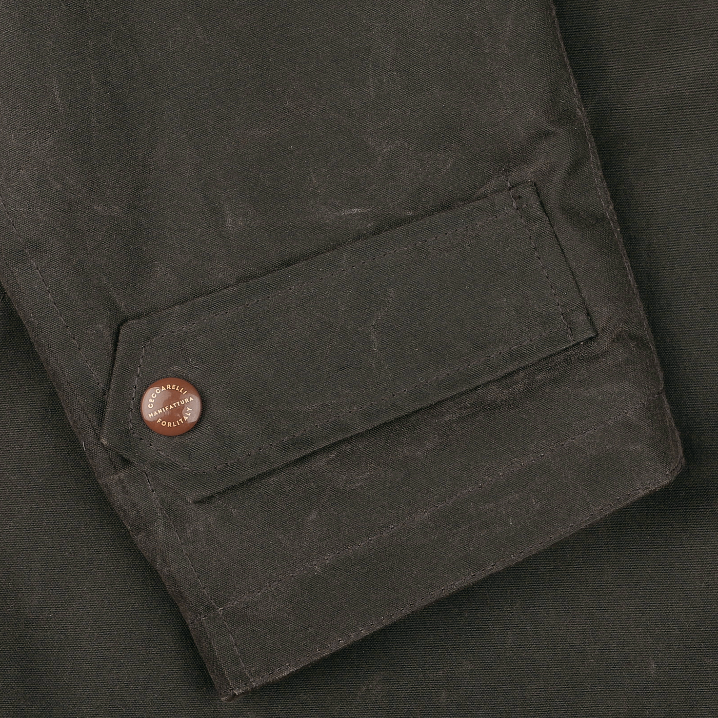 Close-up of a dark green waxed cotton sleeve from the Manifattura Ceccarelli Mountain Parka, showcasing a single brown button and a rectangular pocket flap, exuding the rugged charm of a classic mountain parka.