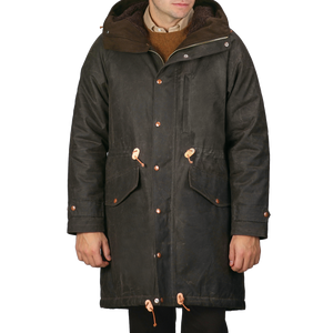 A person wearing the Dark Green Waxed Cotton Mountain Parka by Manifattura Ceccarelli, featuring a long design with a hood, crafted from water-repellent cotton canvas with front pockets and toggle buttons.