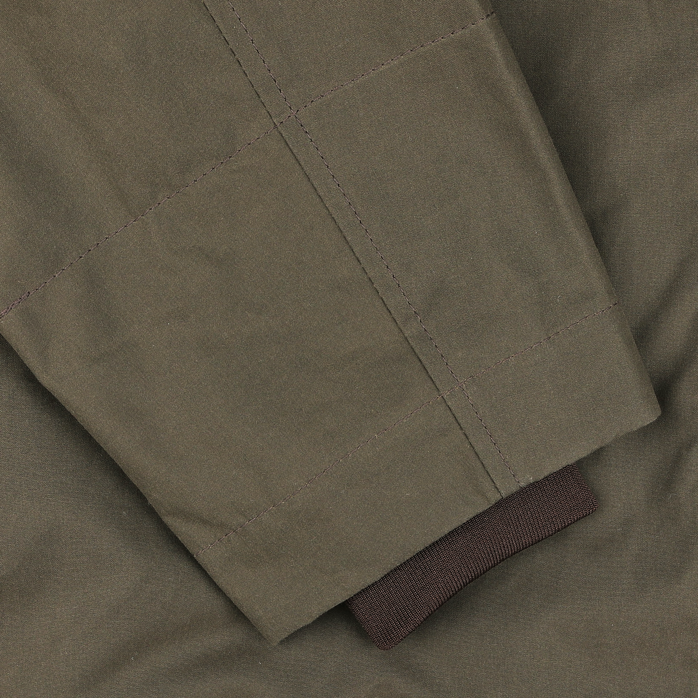 Close-up of a sleeve from the Olive Green Waxed Cotton Blazer Coat by Manifattura Ceccarelli, showcasing fine visible stitching and a contrasting brown knit cuff.