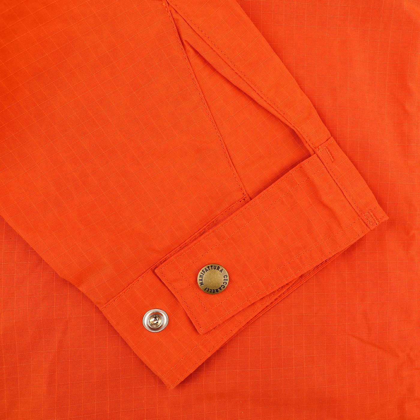 Close-up of an Orange Cotton Nylon Ripstop All Seasons Blazer Coat sleeve by Manifattura Ceccarelli, highlighting a buttoned cuff and a metal button with engraved text.