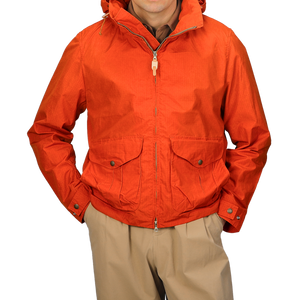 A person is wearing the Manifattura Ceccarelli Orange Cotton Nylon Ripstop All Seasons Blazer Coat with a hood, zipper, and two front pockets over tan pants. The jacket boasts a detachable lining for versatility in different weather conditions.