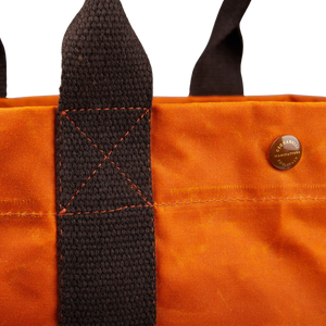 A close up of a Manifattura Ceccarelli Orange Waxed Cotton Tote Bag with dark brown cotton canvas details.