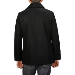 Rear view of a person wearing the Dark Navy Heavy Wool Peacoat by Manifattura Ceccarelli, crafted from a heavy wool blend, and jeans, standing against a plain background.