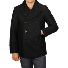 A person in a Manifattura Ceccarelli Dark Navy Heavy Wool Peacoat stands with their right hand in the coat pocket while their left hand rests relaxed by their side. Only the upper body is visible in the image.