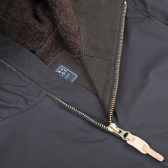 Close-up of a navy blue waxed cotton blazer coat by Manifattura Ceccarelli, featuring a brown fleece lining and a tan zipper pull. Inside the water-repellent jacket, a fabric label with text is visible.