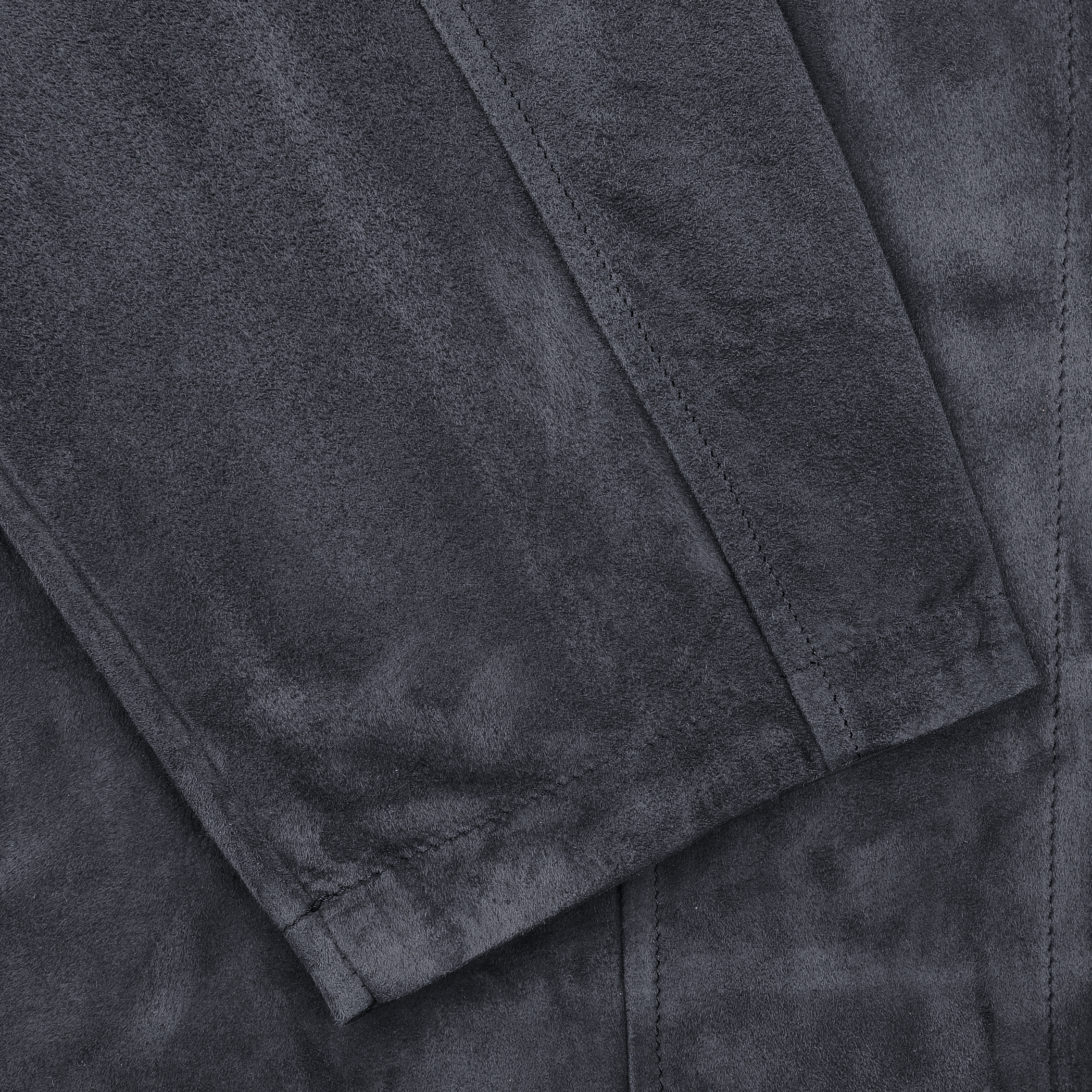 A close-up of the Denim Blue Suede fabric by Manto reveals a textured surface and stitched edges, echoing the quality of a stylish overshirt.