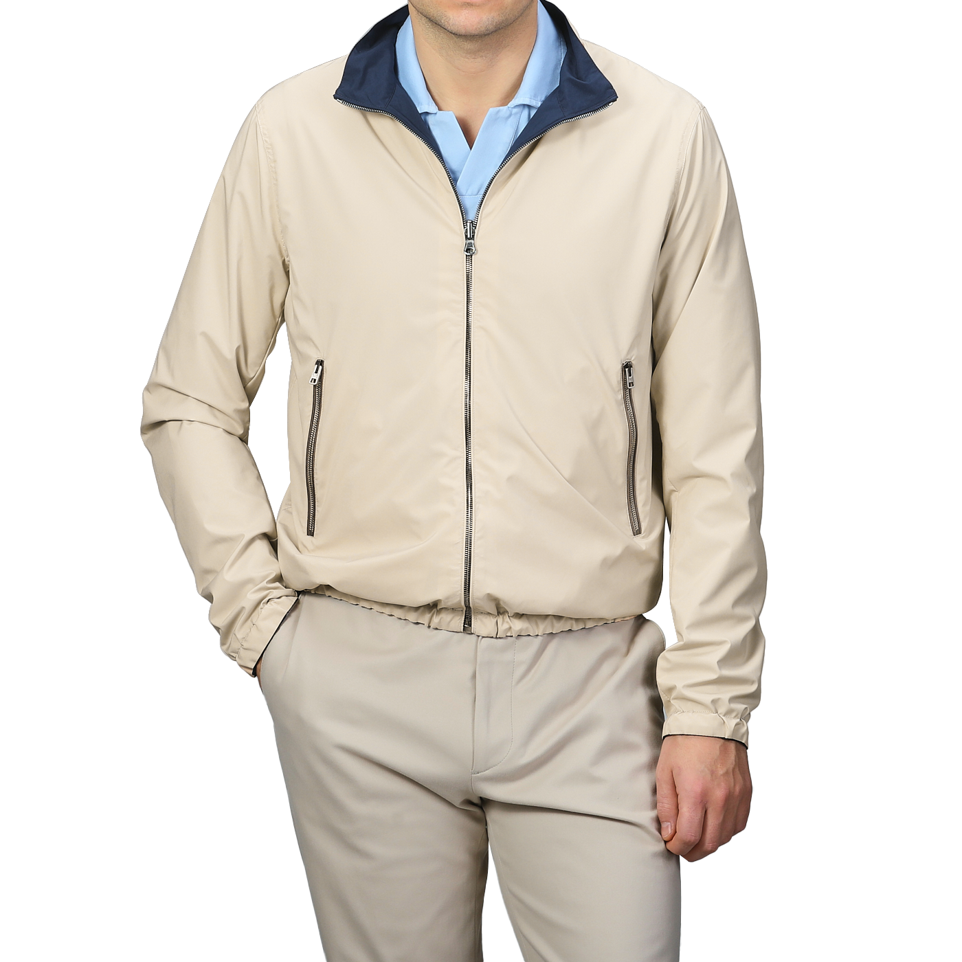 A person in Manto's Navy Beige Reversible Nylon Blouson, with coordinating pants and a blue shirt, stands with one hand in their pocket against a gray background. The sleek slim-fit design enhances the modern aesthetic.