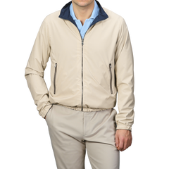 A person in Manto's Navy Beige Reversible Nylon Blouson, with coordinating pants and a blue shirt, stands with one hand in their pocket against a gray background. The sleek slim-fit design enhances the modern aesthetic.