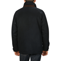 A person wearing a Navy Blue Cashmere Car Coat by Manto and jeans is standing with their back facing the camera against a plain gray background.