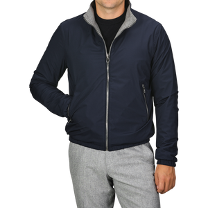 A person dressed in the Manto Navy Grey Cashmere Nylon Reversible Blouson with grey trim and light grey pants. The blouson is zipped up, and the person has their left hand in their pocket, with their face out of view.